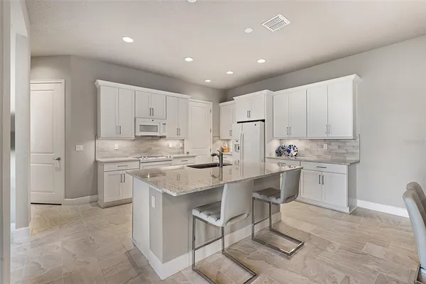 a kitchen with granite countertop a sink stove a refrigerator and white cabinets