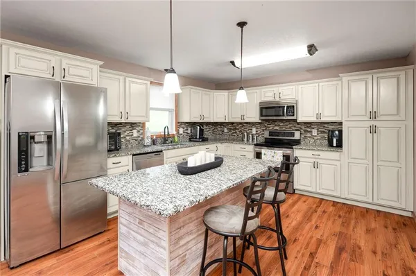 a kitchen with stainless steel appliances granite countertop a sink a stove a refrigerator cabinets and chairs