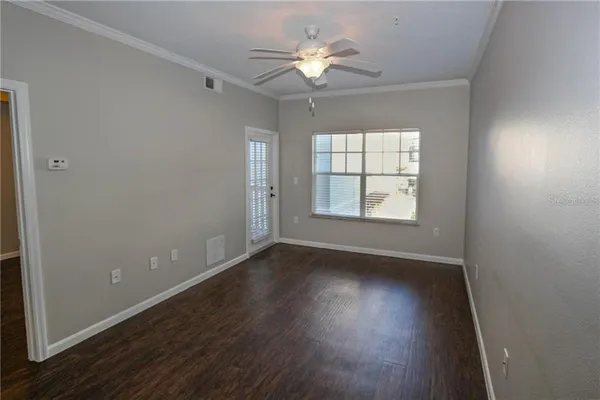 an empty room with wooden floor chandelier fan and windows