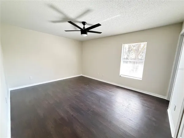 an empty room with wooden floor fan and windows
