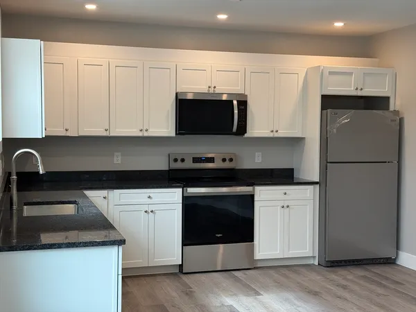 a kitchen with granite countertop a refrigerator stove and white cabinets