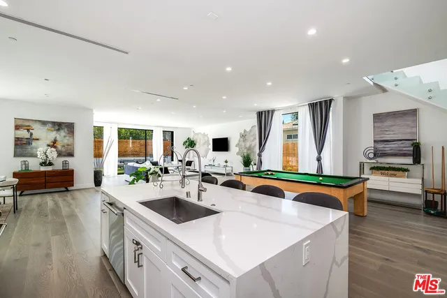 a view of a kitchen with kitchen island a stove a sink a refrigerator and a dining table with wooden floor