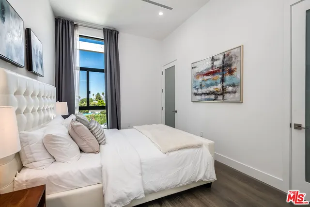 a bedroom with a bed painting on wall and a large window