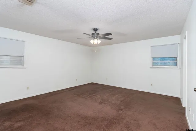 an empty room with a chandelier fan and windows