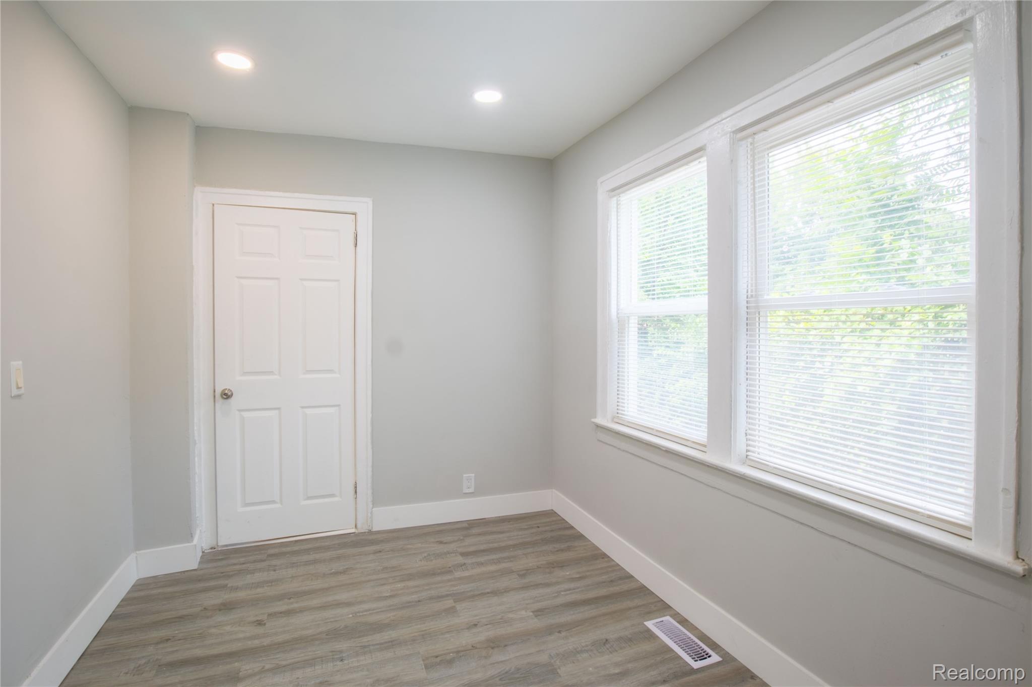 633 Perry Street Pontiac, MI 48342 - Photo 9 of 26 Bright room featuring two large windows with horizontal blinds, wood-finish flooring, recessed ceiling lighting, and a six-panel interior door
