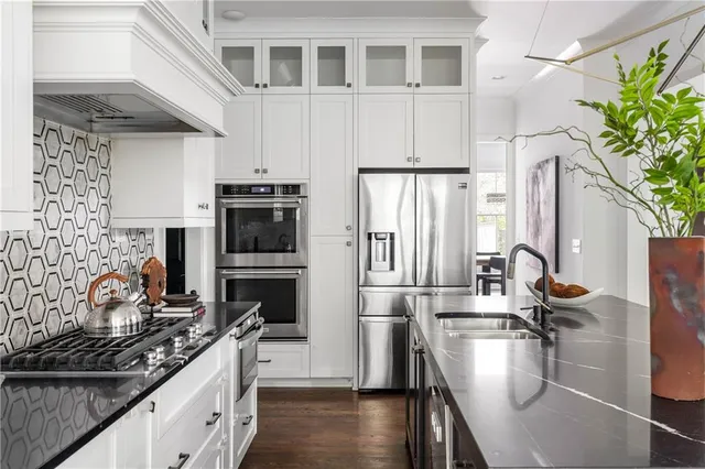 a kitchen with stainless steel appliances a stove a sink dishwasher a refrigerator white cabinets and wooden floor