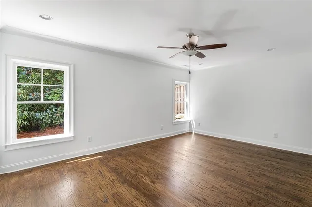 an empty room with wooden floor ceiling fan and windows
