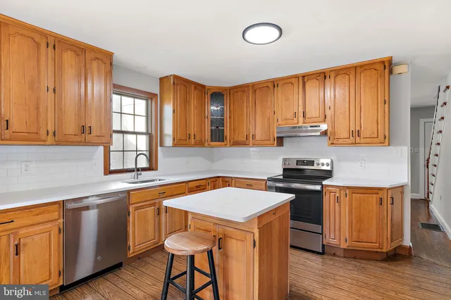 a kitchen with stainless steel appliances granite countertop wooden cabinets a stove a sink and dishwasher with wooden floor