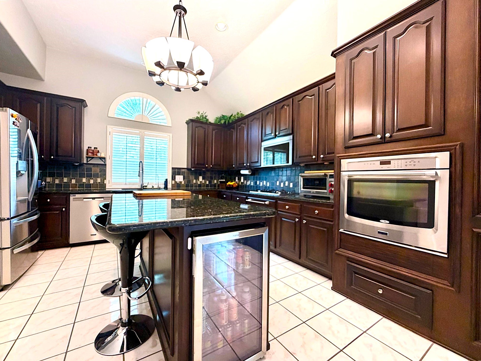 24818 Haverford Road Spring, TX 77389 - Photo 23 of 45 This kitchen features elegant dark wood cabinetry, a large island with bar seating, stainless steel appliances, and a built-in oven. It boasts a high ceiling with a stylish light fixture and a large window for natural light. Perfect for cooking and entertaining.