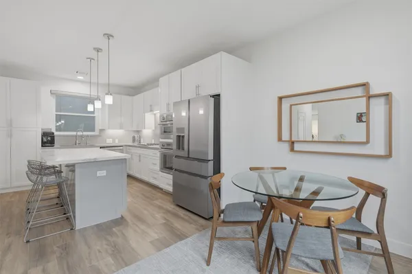 a kitchen with stainless steel appliances kitchen island granite countertop a dining table chairs and a refrigerator