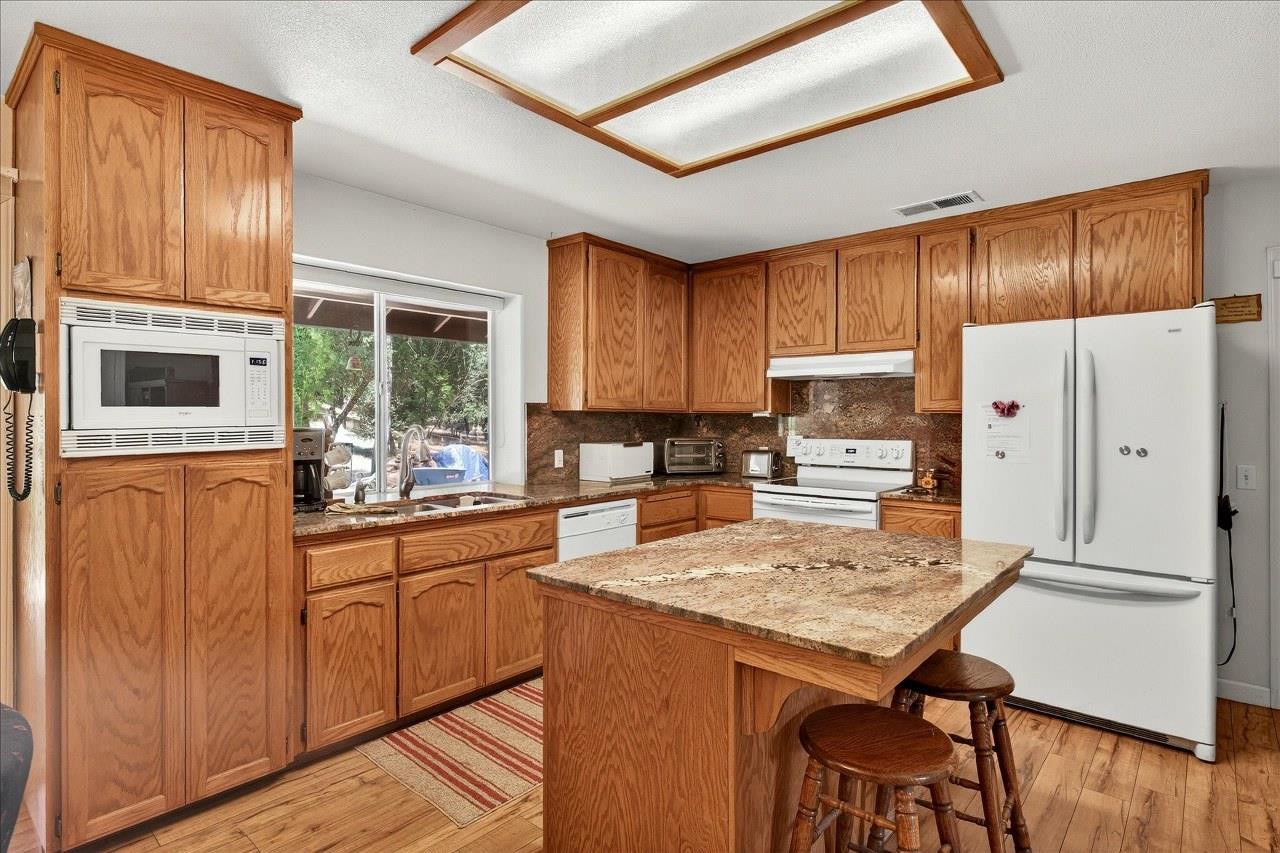 38090 Wortham Road Oakhurst, CA 93644 - Photo 19 of 54 a kitchen with granite countertop wooden cabinets a stove a oven a sink and dishwasher with wooden floor
