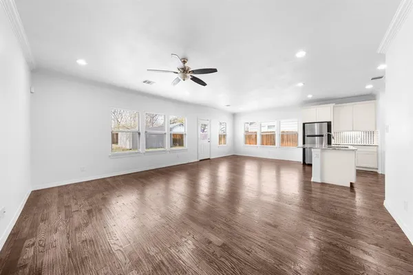a view of empty room with wooden floor and a kitchen