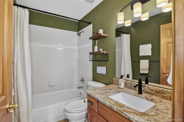 a bathroom with a granite countertop bathtub shower sink vanity and toilet