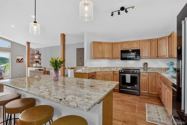 a kitchen with stainless steel appliances granite countertop a stove top oven a sink a dining table and chairs with wooden floor