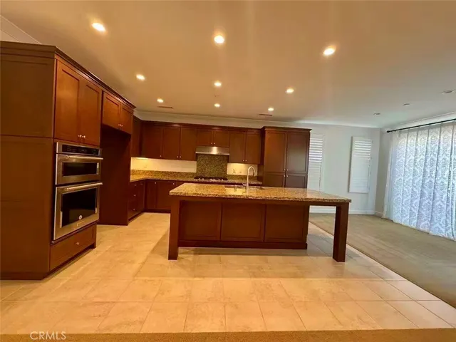 a kitchen with stainless steel appliances kitchen island granite countertop a refrigerator a stove and a sink with wooden cabinets