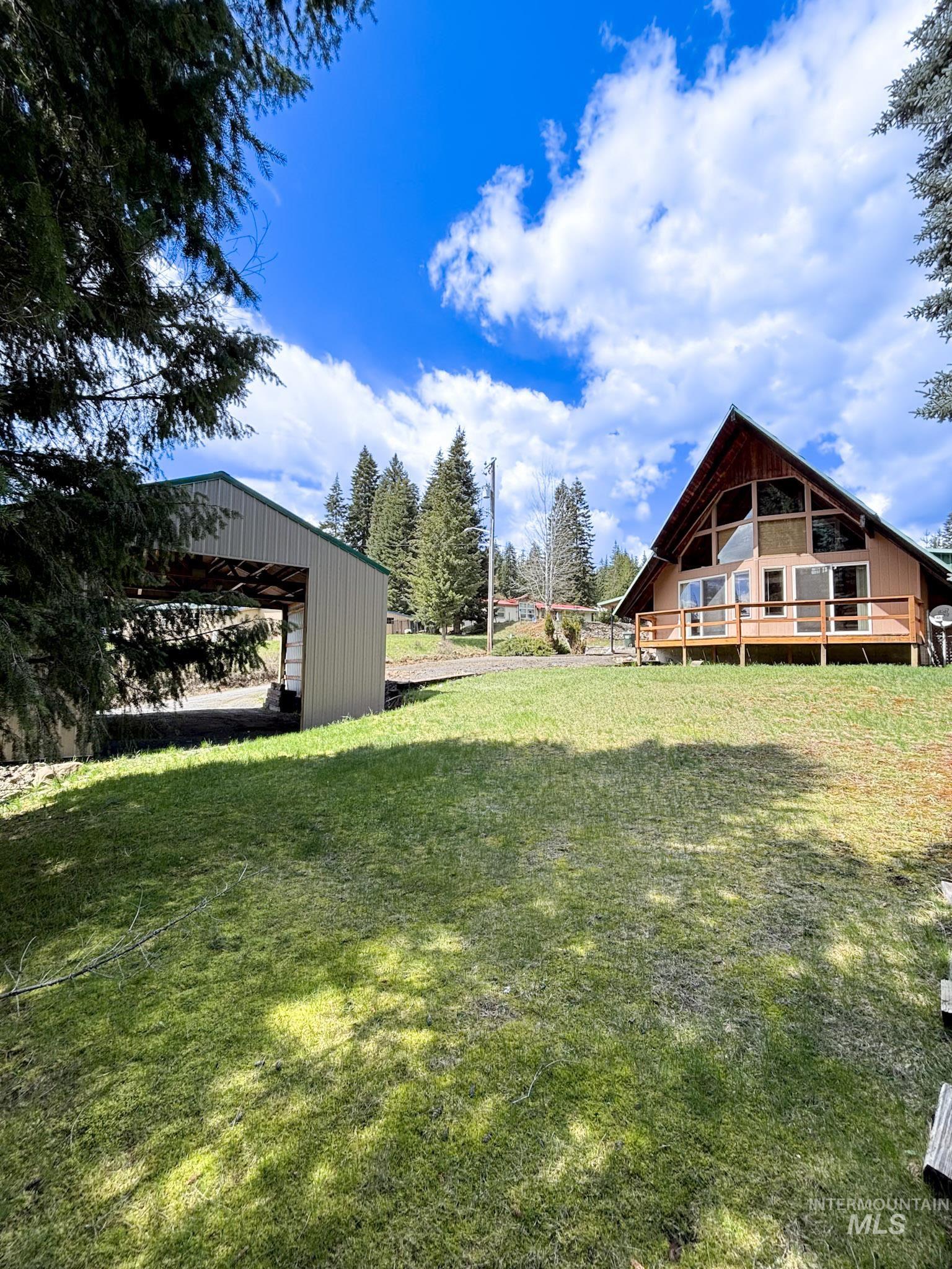A-frame dwelling featuring an expansive front deck, large windows, and a detached metal carport structure