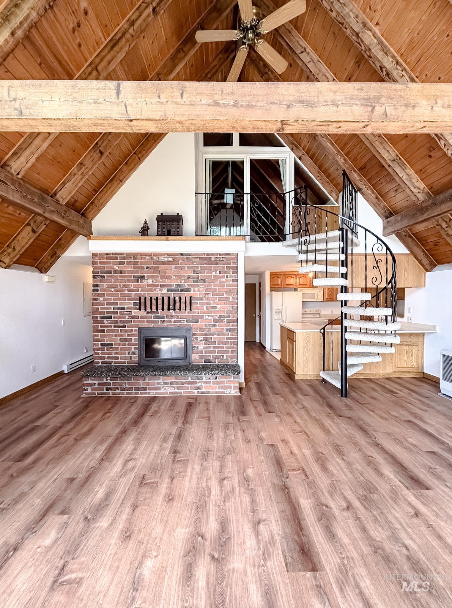 302 Rossiter Court Pierce, ID 83546 - Photo 16 of 30 Vaulted wood-paneled ceilings with exposed beams, wood-finish flooring, a spiral staircase with ornate ironwork, a brick fireplace with a hearth, and a functional ceiling fan