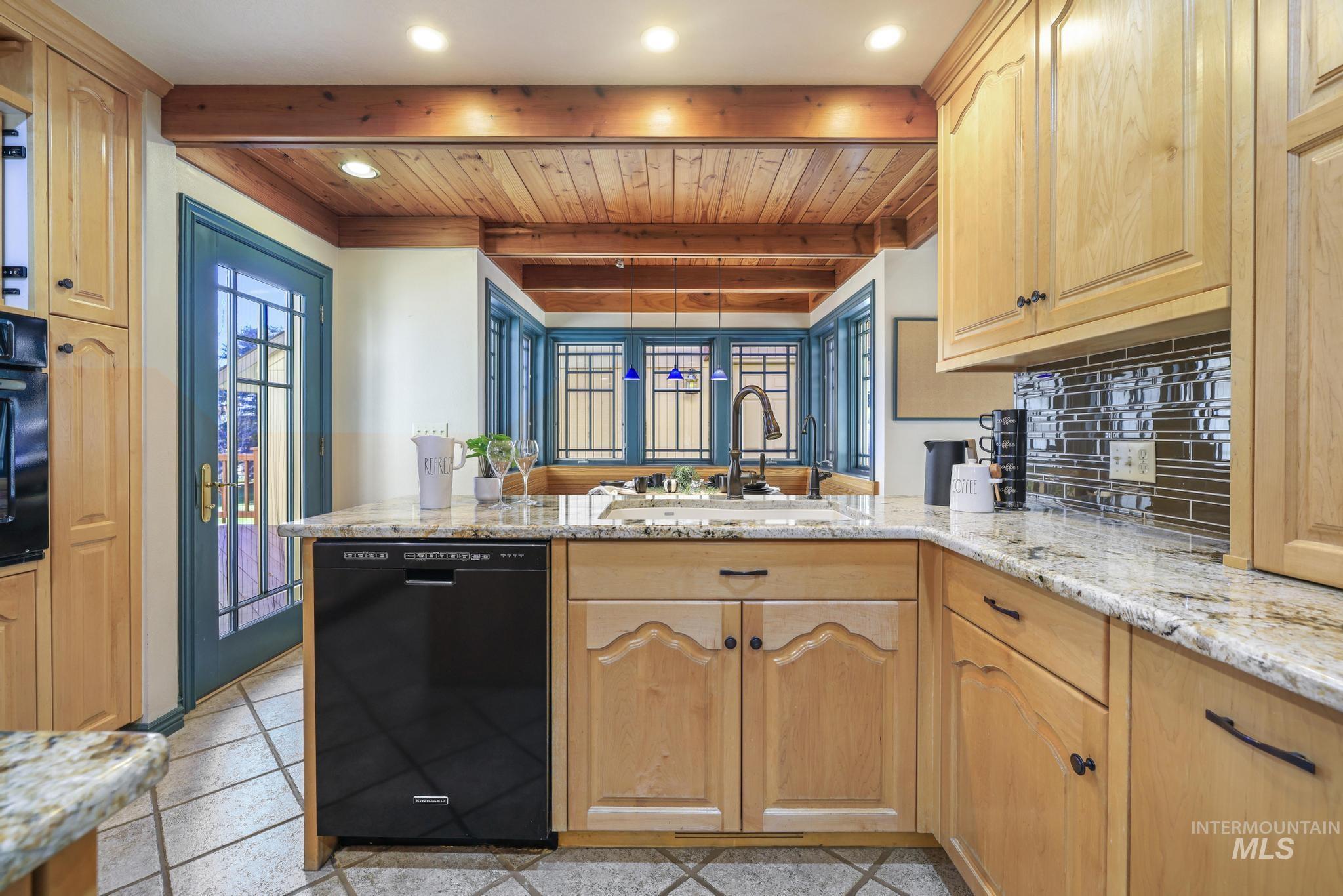 1172 Hankins Road North Twin Falls, ID 83301 - Photo 17 of 49 Kitchen with light stone counters, black appliances, a peninsula, light wood finish cabinets, and beamed ceiling