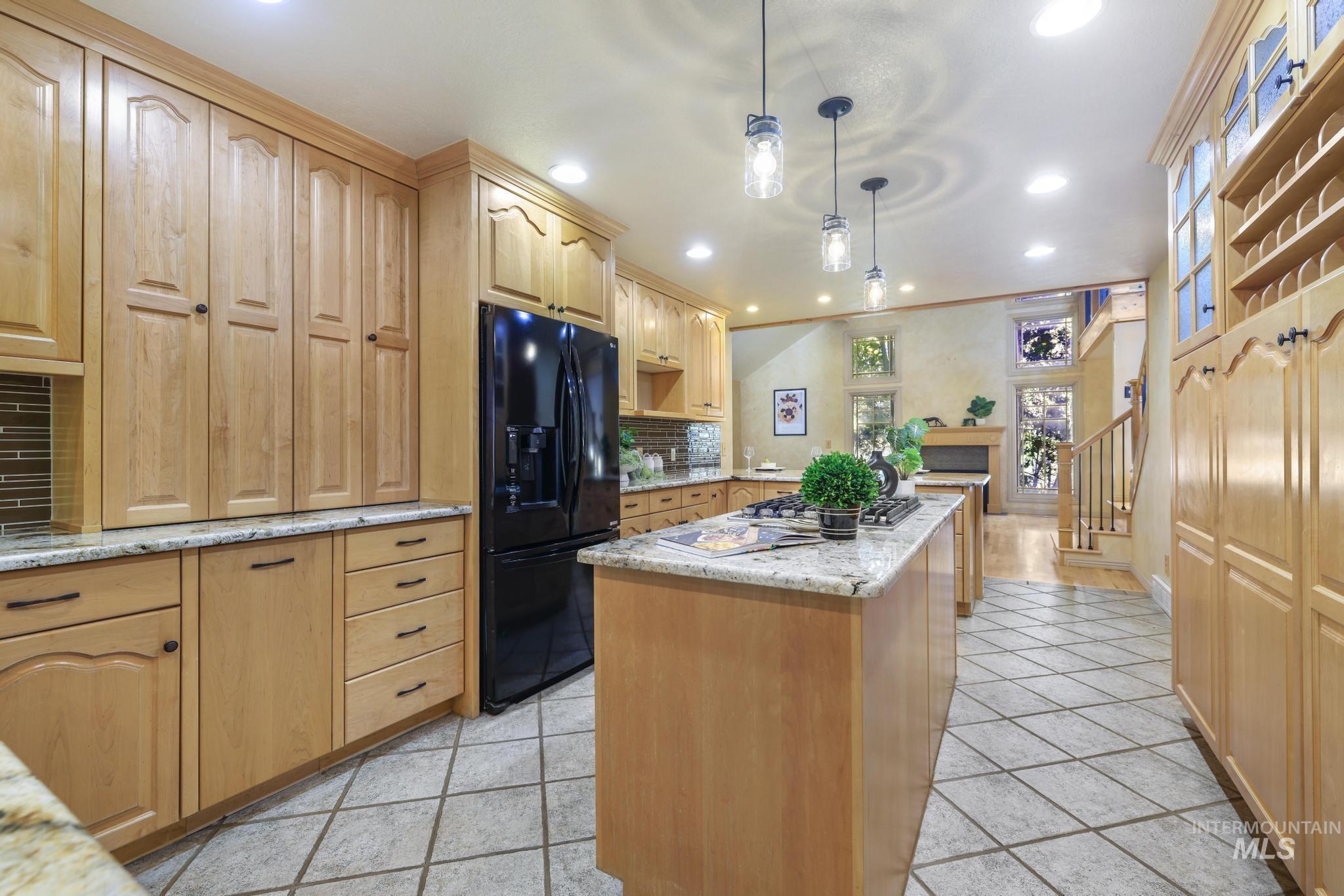 1172 Hankins Road North Twin Falls, ID 83301 - Photo 18 of 49 Kitchen featuring a center island, black fridge, light wood finish cabinets, light stone counters, and decorative backsplash