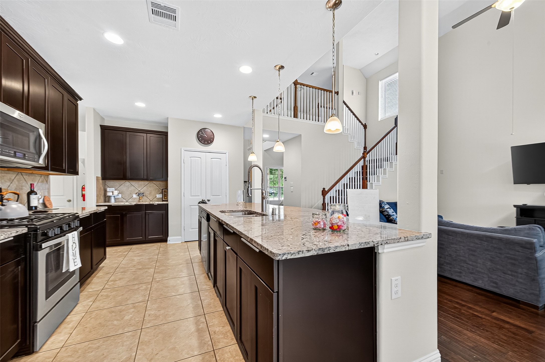 8107 Lockridge Terrace Lane Cypress, TX 77433 - Photo 22 of 50 This final view of the open kitchen showcases its seamless integration into the heart of the home. From the gleaming granite island, your eyes are drawn to the warm wood staircase and the airy two-story living area beyond—perfectly connecting form and function. With clear sightlines to the family room and upstairs balcony, this layout fosters togetherness and ease of living.