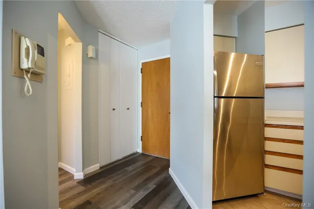 a view of a refrigerator in kitchen and an empty room with wooden floor