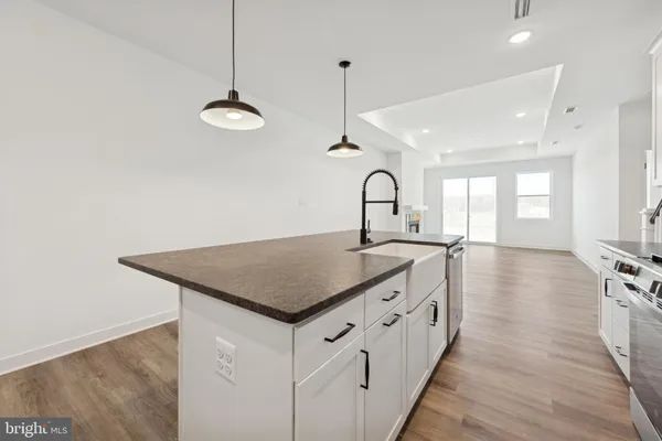 a kitchen with stainless steel appliances granite countertop a sink a stove a refrigerator and white cabinets with wooden floor
