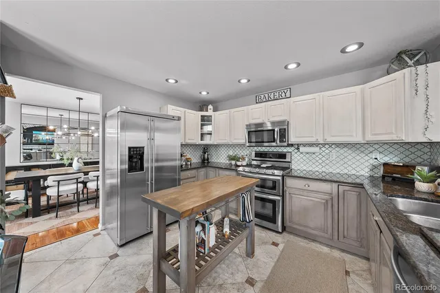 a kitchen with stainless steel appliances granite countertop a stove top oven a sink a refrigerator white cabinets and chairs