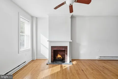 a view of an empty room with wooden floor fireplace and a window