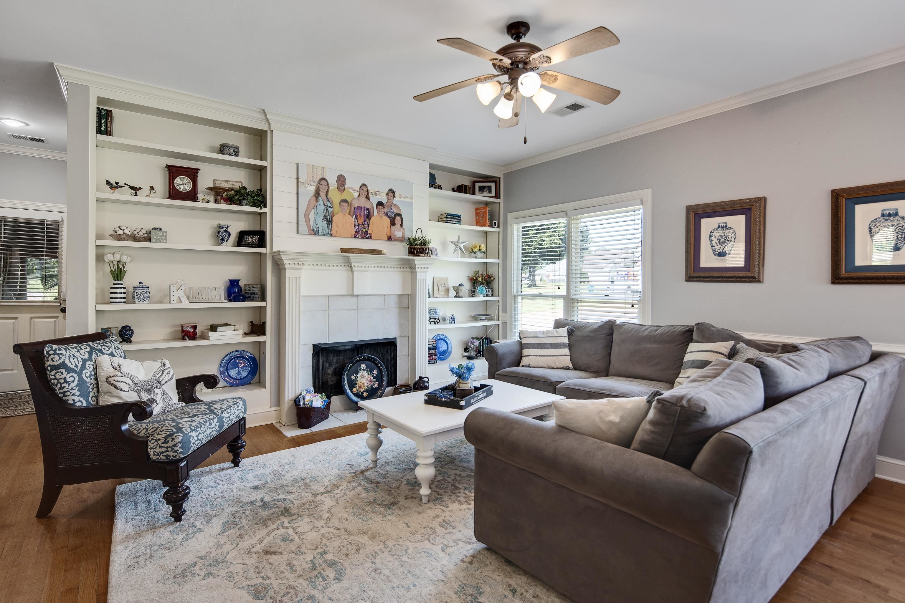 1323 Colbert Cove Collierville, TN 38017 - Photo 19 of 40 Living room featuring a tile fireplace, crown molding, ceiling fan, built in features, and hardwood / wood-style flooring