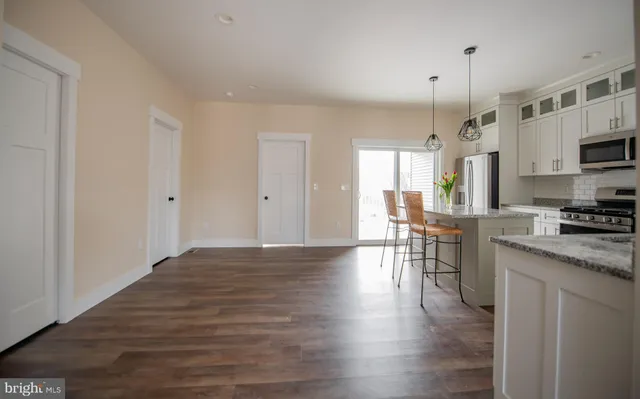 a open kitchen with stainless steel appliances granite countertop a stove a sink a refrigerator and white cabinets with wooden floor