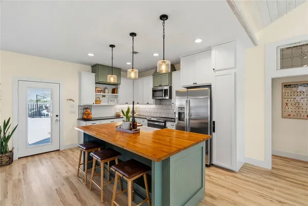a kitchen with stainless steel appliances granite countertop a kitchen island a stove a refrigerator a sink a dining table and chairs with wooden floor