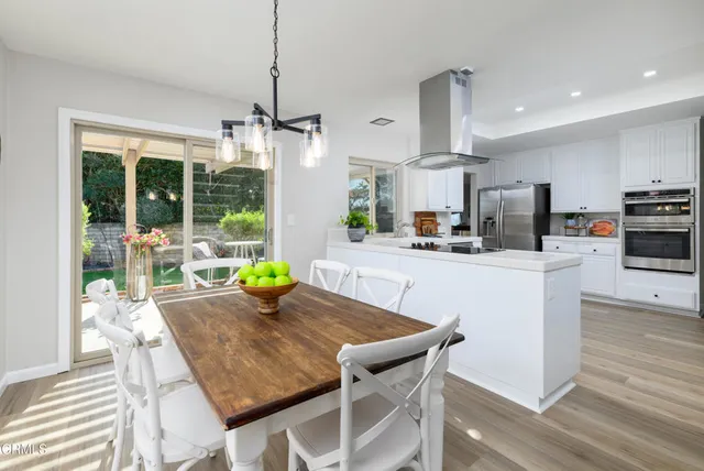 a kitchen with stainless steel appliances kitchen island granite countertop a stove a refrigerator a sink a dining table and chairs with wooden floor
