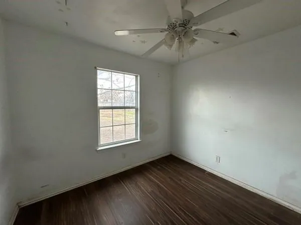 an empty room with wooden floor fan and windows