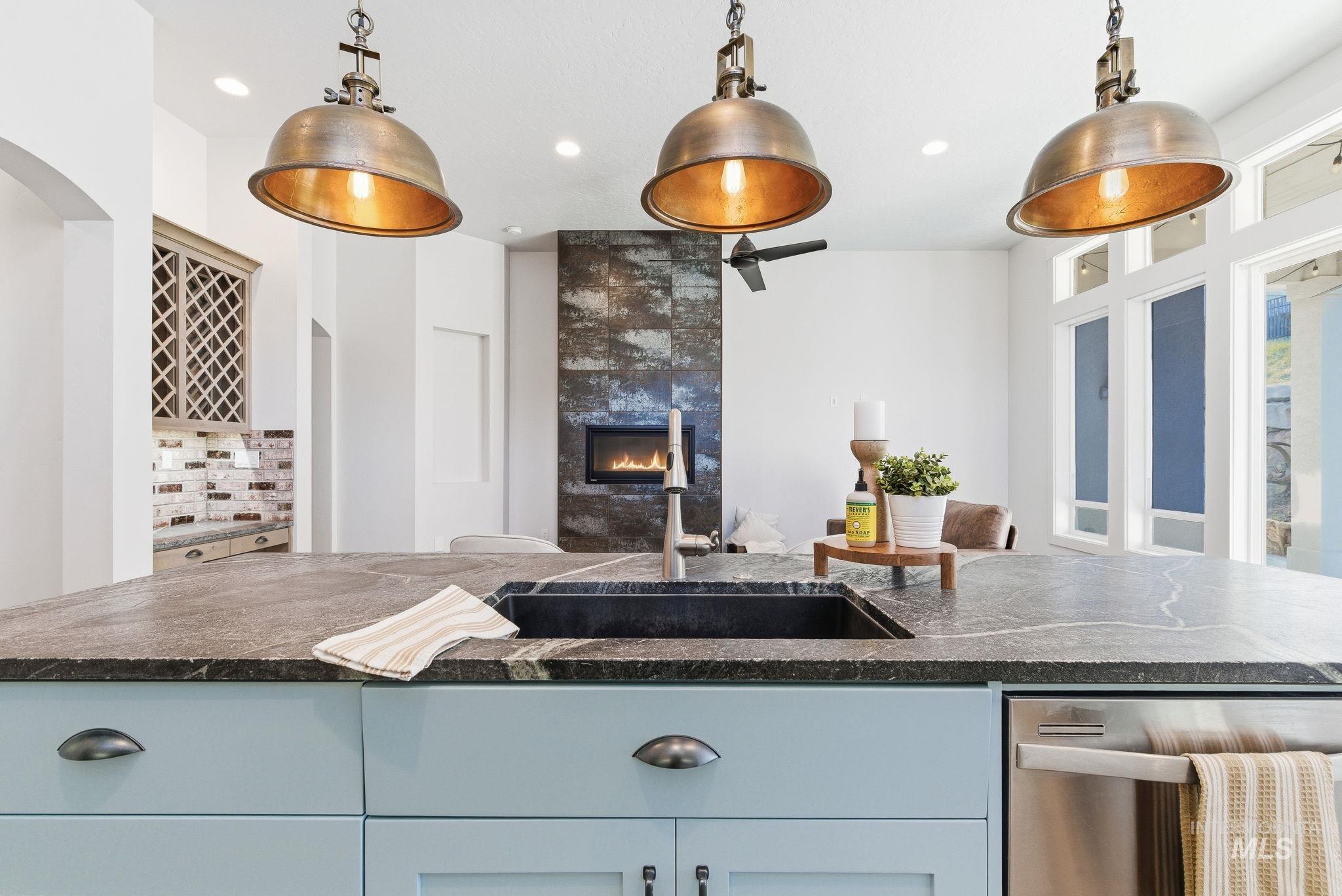 1013 East Radiant Ridge Drive Meridian, ID 83642 - Photo 12 of 36 Kitchen with hanging light fixtures, dishwasher, dark stone countertops, a tile fireplace, and arched walkways
