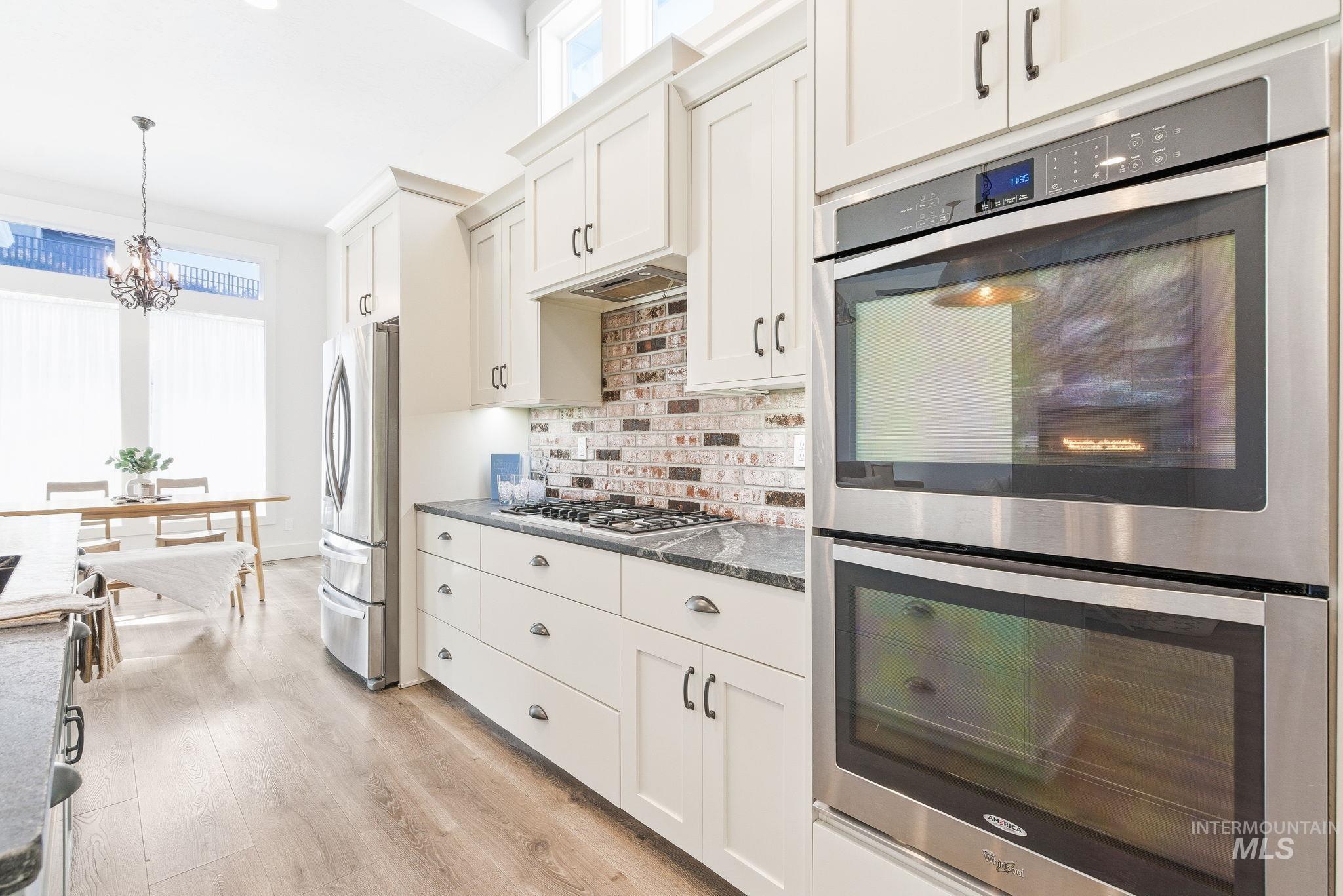 1013 East Radiant Ridge Drive Meridian, ID 83642 - Photo 13 of 36 Kitchen featuring stainless steel appliances, light wood finished floors, white cabinetry, hanging light fixtures, and a chandelier