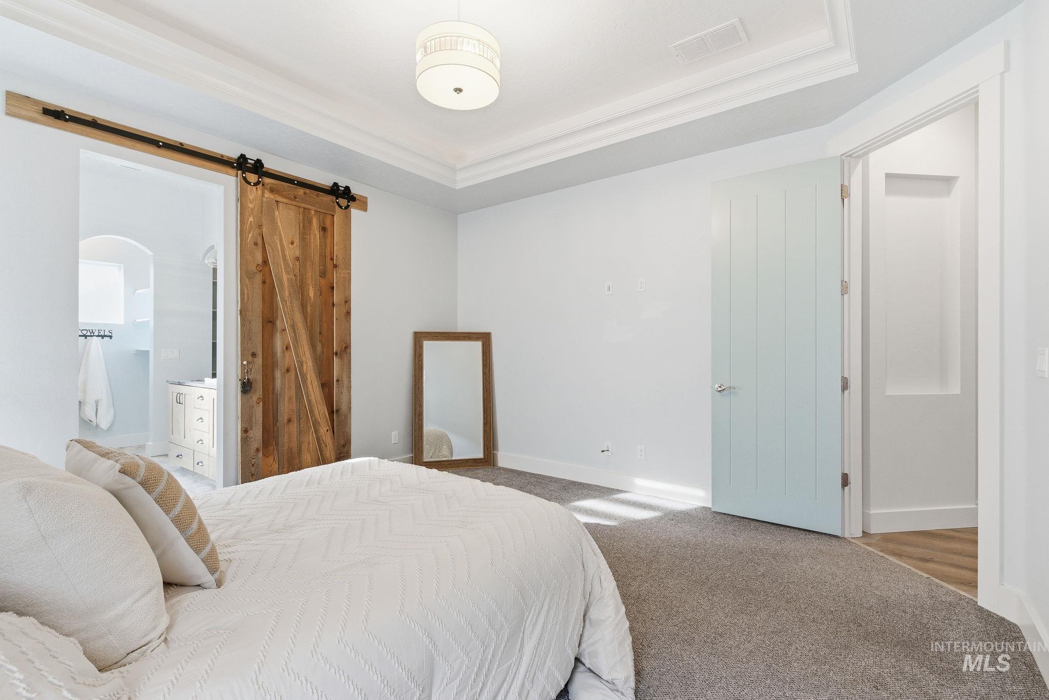 1013 East Radiant Ridge Drive Meridian, ID 83642 - Photo 22 of 36 Carpeted bedroom featuring a barn door, connected bathroom, and a raised ceiling