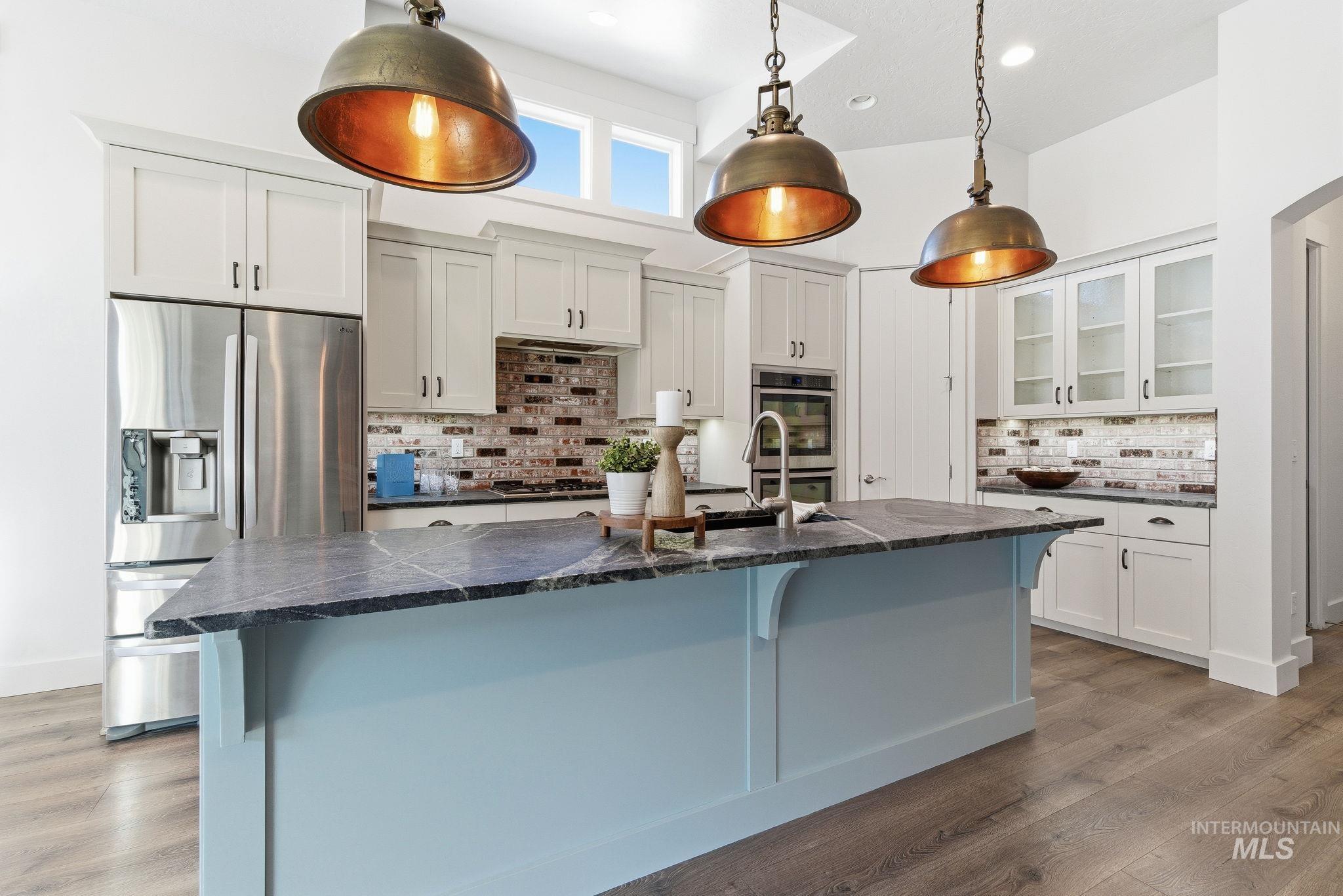 1013 East Radiant Ridge Drive Meridian, ID 83642 - Photo 9 of 36 Kitchen featuring white cabinets, appliances with stainless steel finishes, light wood finished floors, pendant lighting, and a center island with sink