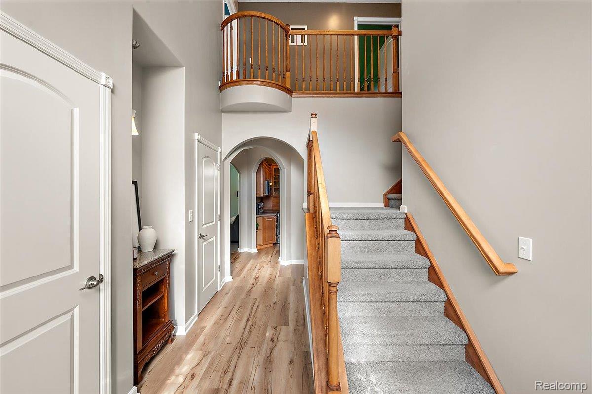 5035 Hidden Ridge Road Metamora, MI 48455 - Photo 2 of 62 Two-story foyer featuring wood-finish flooring, arched doorways, a carpeted staircase with wood banister, and an upper-level balcony with wood railing