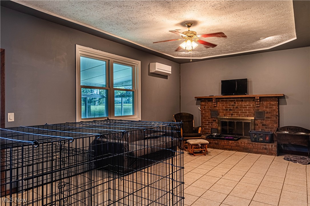 16974 Hawley Road Oberlin, OH 44074 - Photo 9 of 42 Living area featuring a textured ceiling, light tile patterned floors, a brick fireplace, a ceiling fan, and a wall unit AC