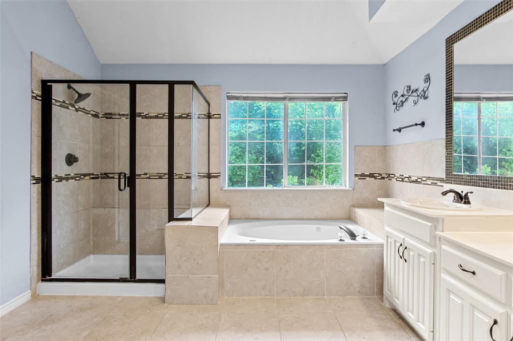 2604 Ridgewood Drive Plano, TX 75074 - Photo 22 of 35 Bathroom featuring a walk-in shower with dark-framed glass enclosure, a built-in jetted tub, a vanity with white cabinetry and a solid surface countertop, and a large window