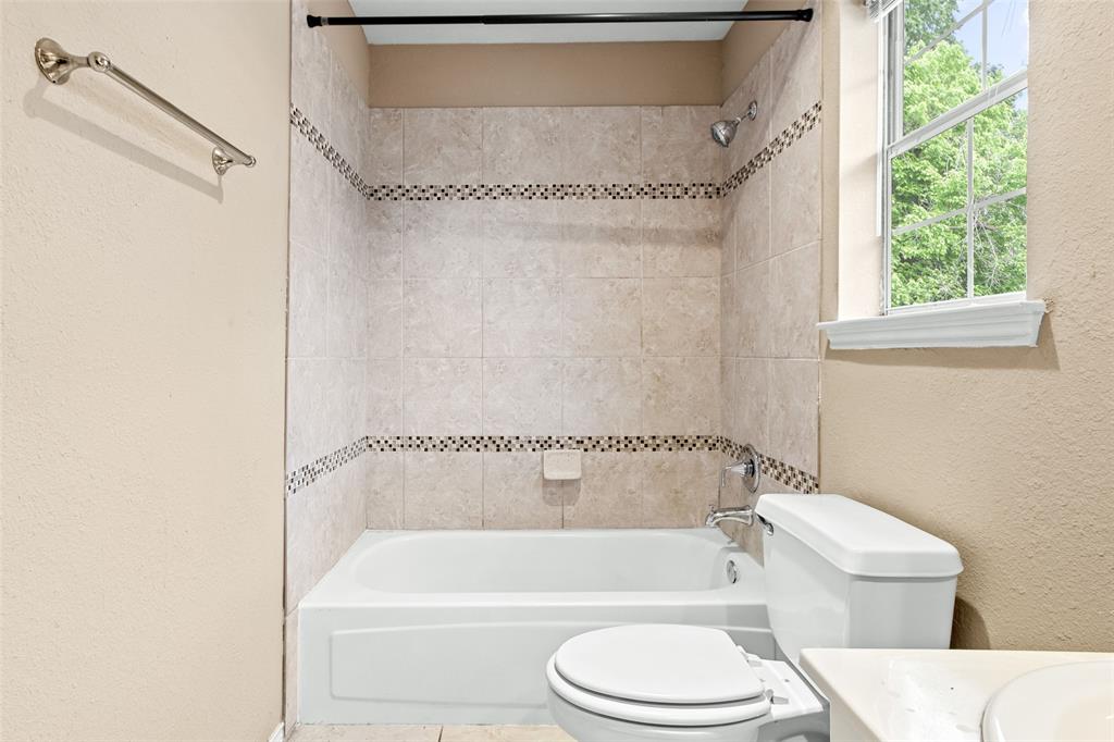 2604 Ridgewood Drive Plano, TX 75074 - Photo 28 of 35 Bathroom featuring a white bathtub, ceramic tile surround with decorative mosaic accents, and a window with white trim