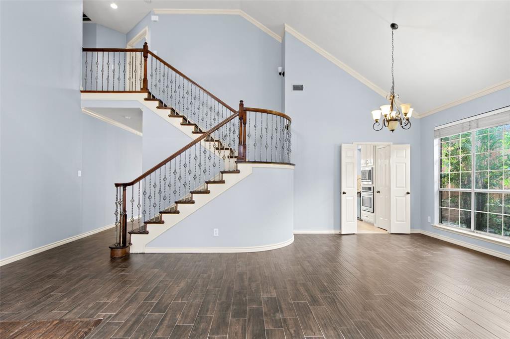 2604 Ridgewood Drive Plano, TX 75074 - Photo 8 of 35 Vaulted ceiling entry featuring a grand staircase with wrought iron balusters and wood handrails, wood-finish flooring, a multi-pane window with exterior landscaping visible, and bifold doors opening to a kitchen space