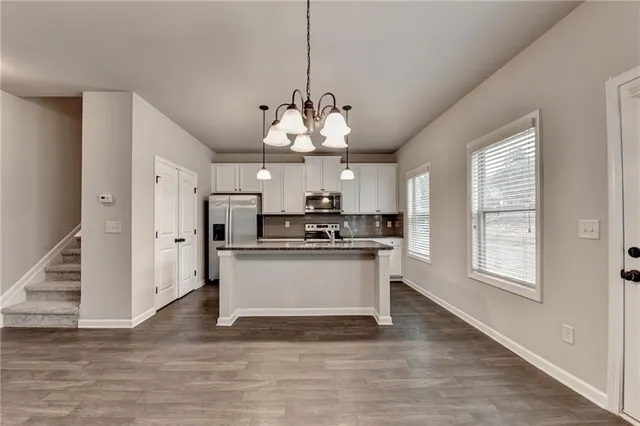 a kitchen with stainless steel appliances granite countertop a stove a sink dishwasher a refrigerator and white cabinets with wooden floor