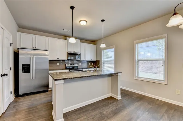 a kitchen with stainless steel appliances granite countertop a refrigerator a sink dishwasher a stove and white cabinets with wooden floor