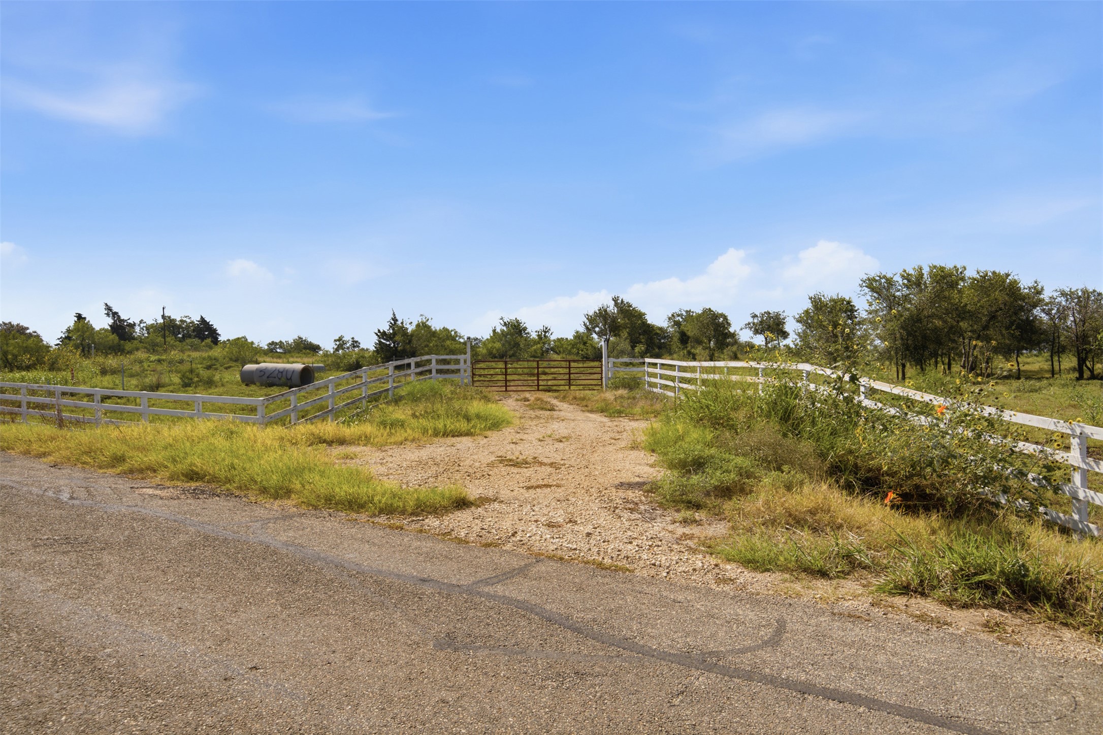 3280 County Road 466 Elgin, TX 78621 - Photo 8 of 13 A rural landscape featuring a white fence and an entrance gate leads into a verdant field.