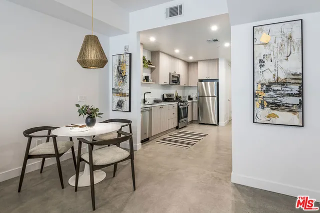 a kitchen with stainless steel appliances kitchen island granite countertop a dining table chairs and a refrigerator