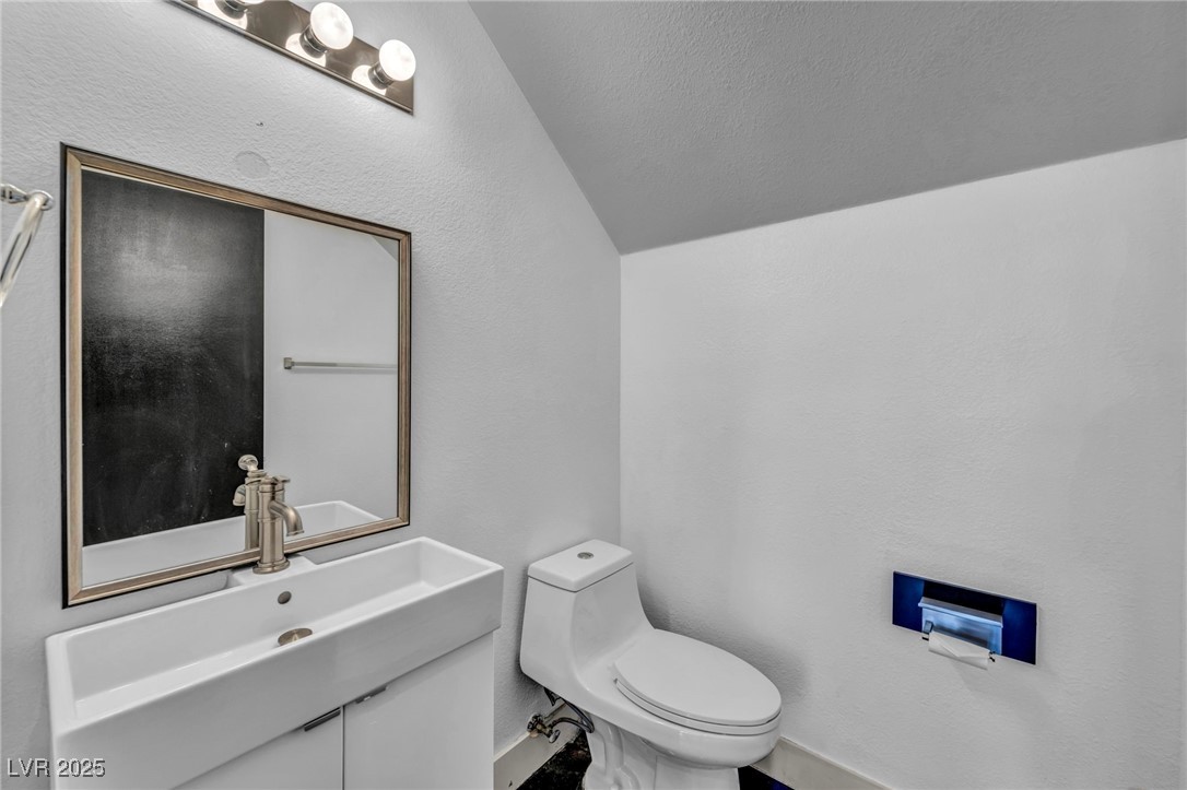 7308 Alpine Ridge Street Las Vegas, NV 89131 - Photo 15 of 47 Half bath with lofted ceiling, a textured wall, vanity, and toilet