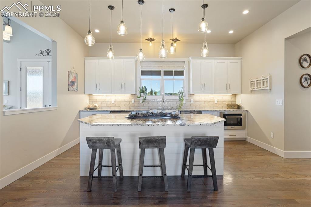 16835 Goshawk Road Colorado Springs, CO 80908 - Photo 7 of 50 a kitchen with kitchen island granite countertop a dining table chairs and white cabinets