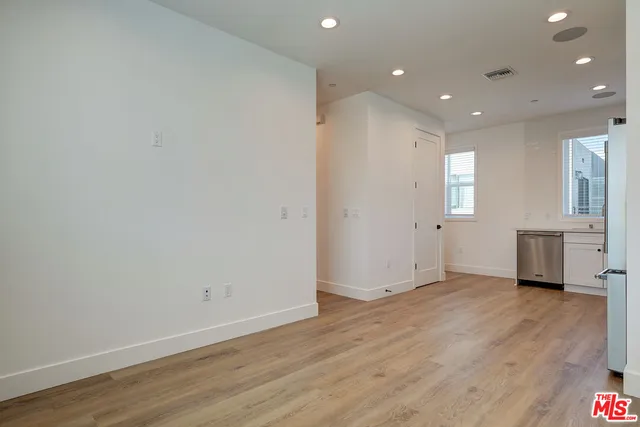 a view of an empty room with wooden floor and a kitchen