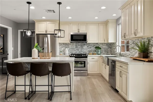 a kitchen with stainless steel appliances kitchen island granite countertop a stove top oven a sink dishwasher a refrigerator and white cabinets with wooden floor